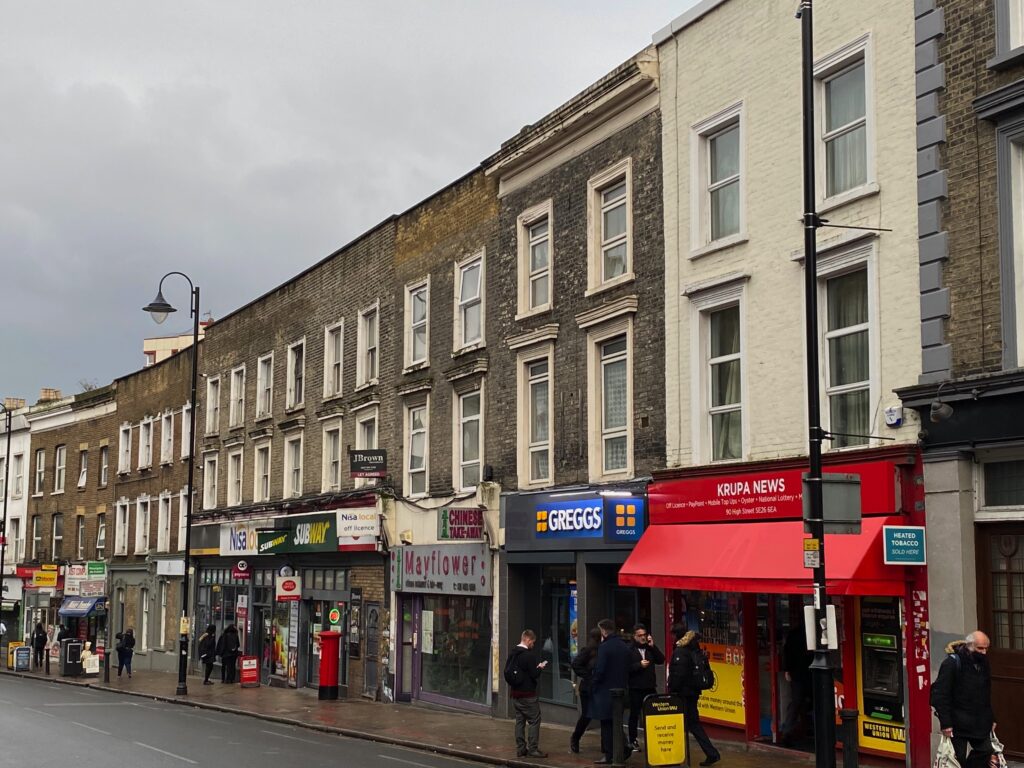 A view down South Norwood High Street showing a row of terraced buildings with shopfronts on each ground floor.