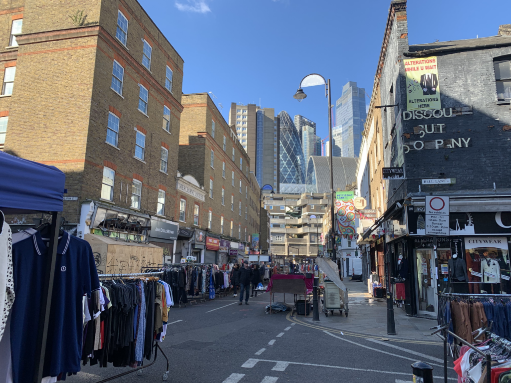 A view down historic Wentworth Street in Tower Hamlets towards the City of London's skyscrapers. Market Stalls extend down the street.