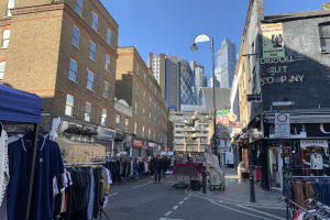 A view down historic Wentworth Street in Tower Hamlets towards the City of London's skyscrapers. Market Stalls extend down the street.